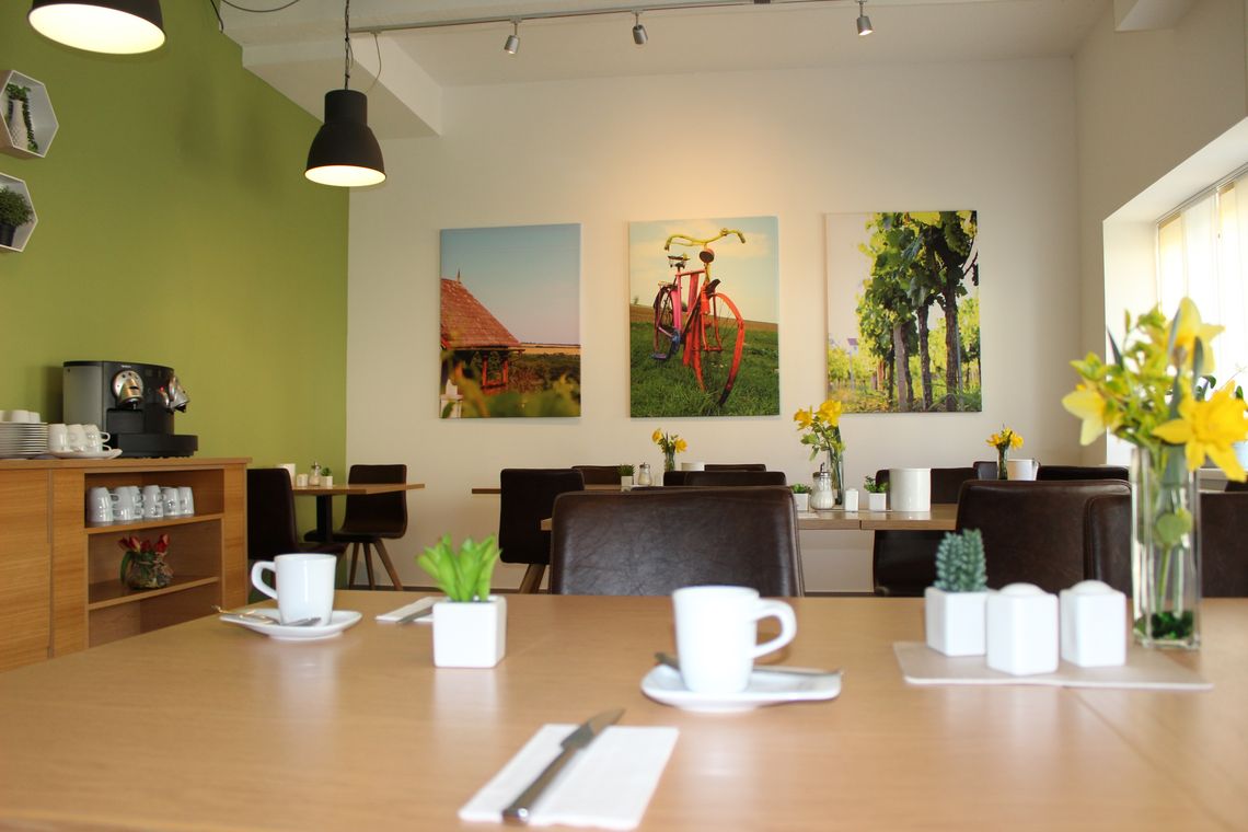 Frühstücksraum von innen, gedeckte Tische, Kaffeemaschine und Bilder an Wand