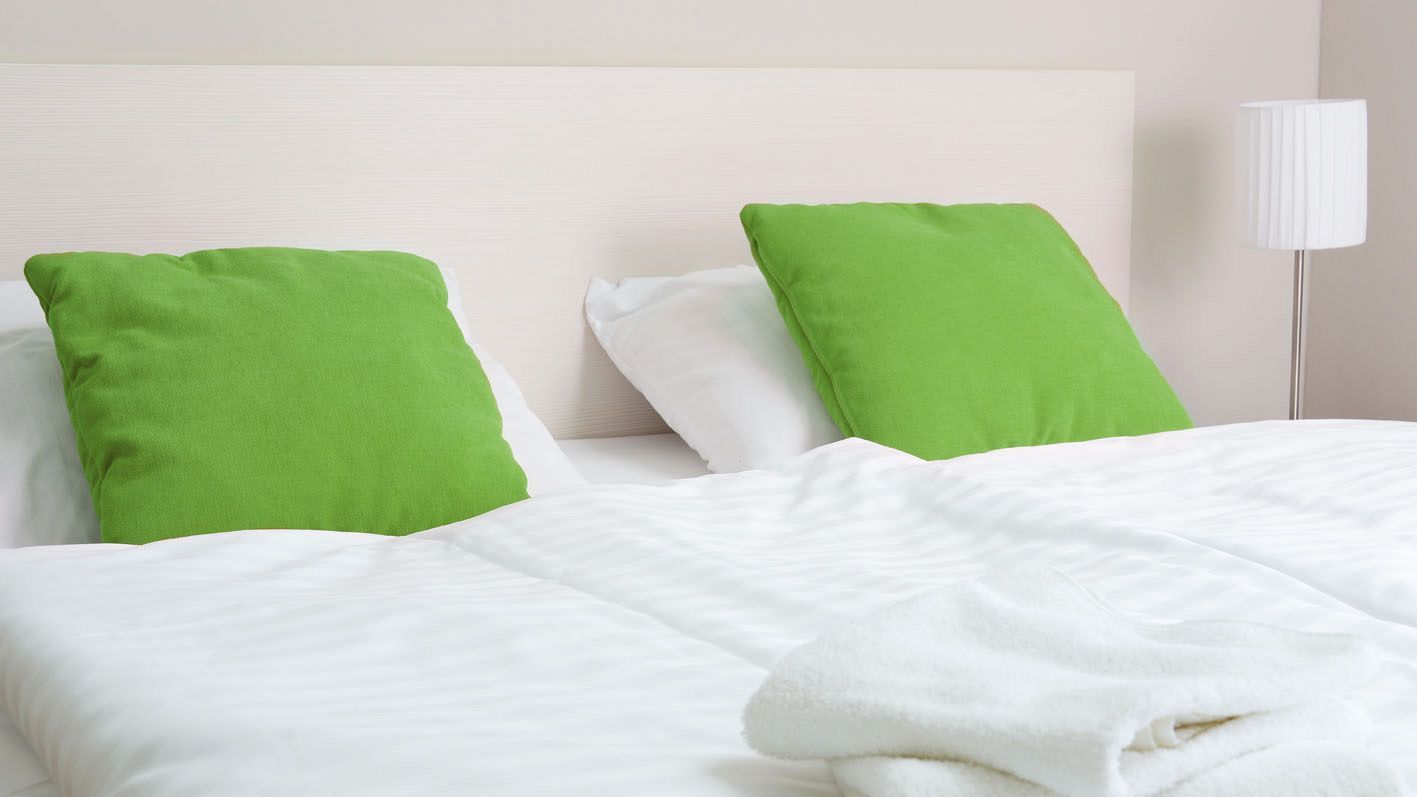 Ein Doppelbett mit zwei weißen und zwei grünen Polstern